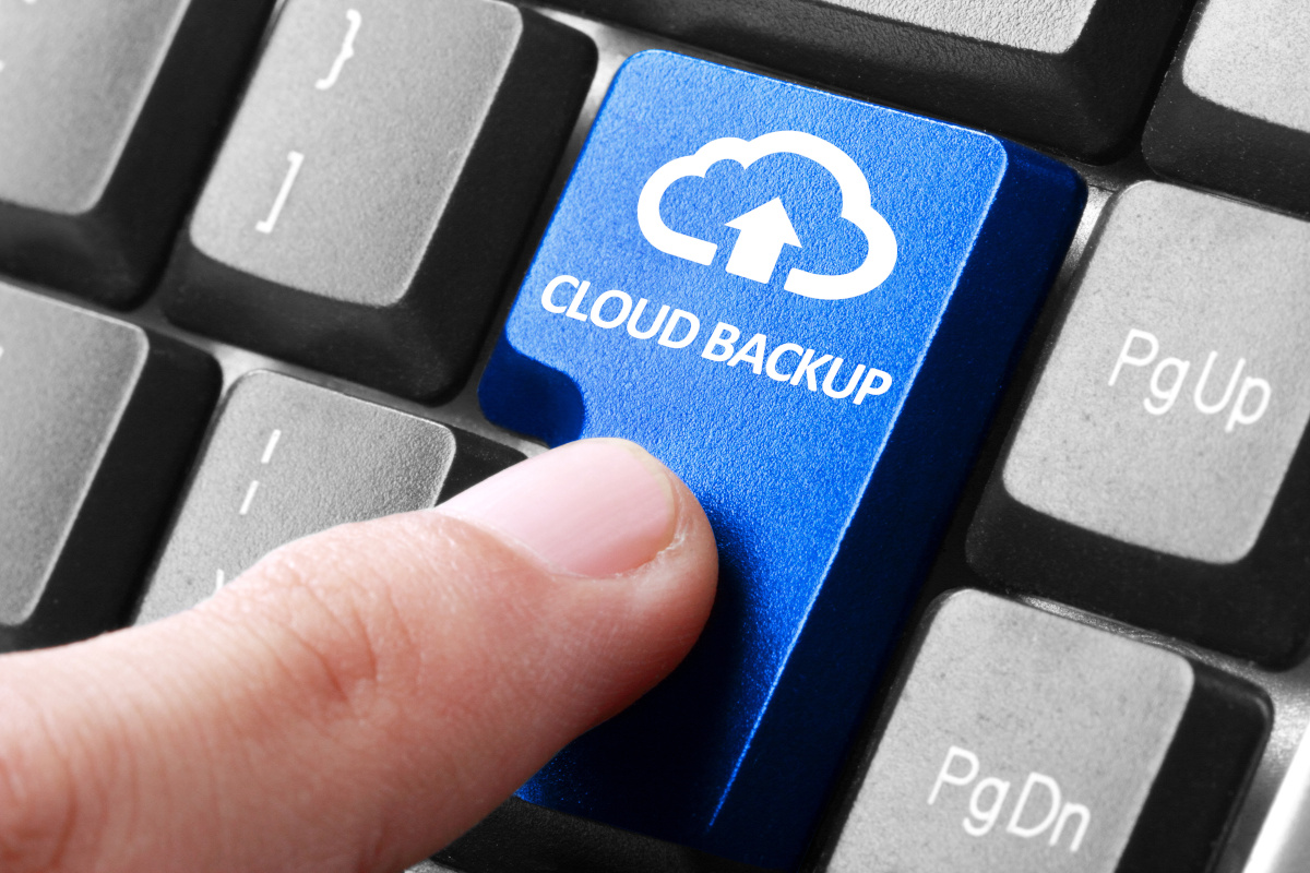 A person's finger hovering over a blue keyboard button that says 'Cloud Backup'