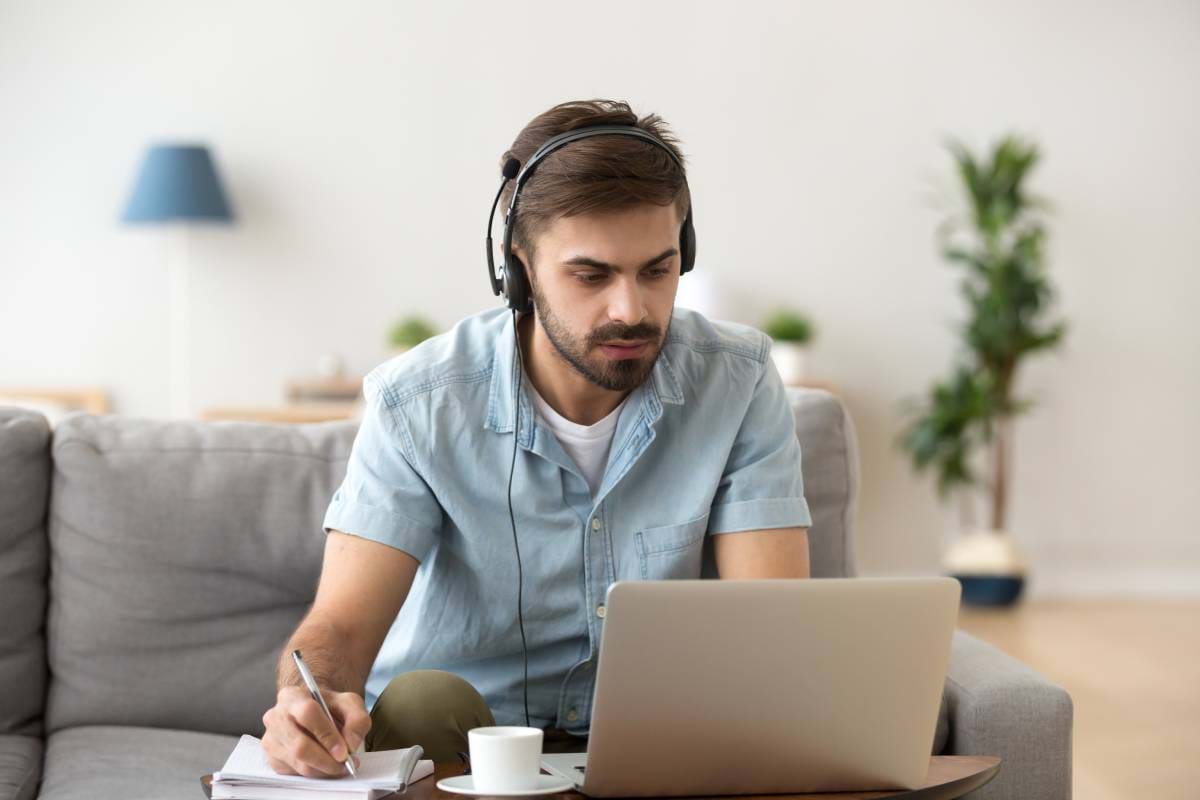 A man working from home using a headset and writing in a notepad